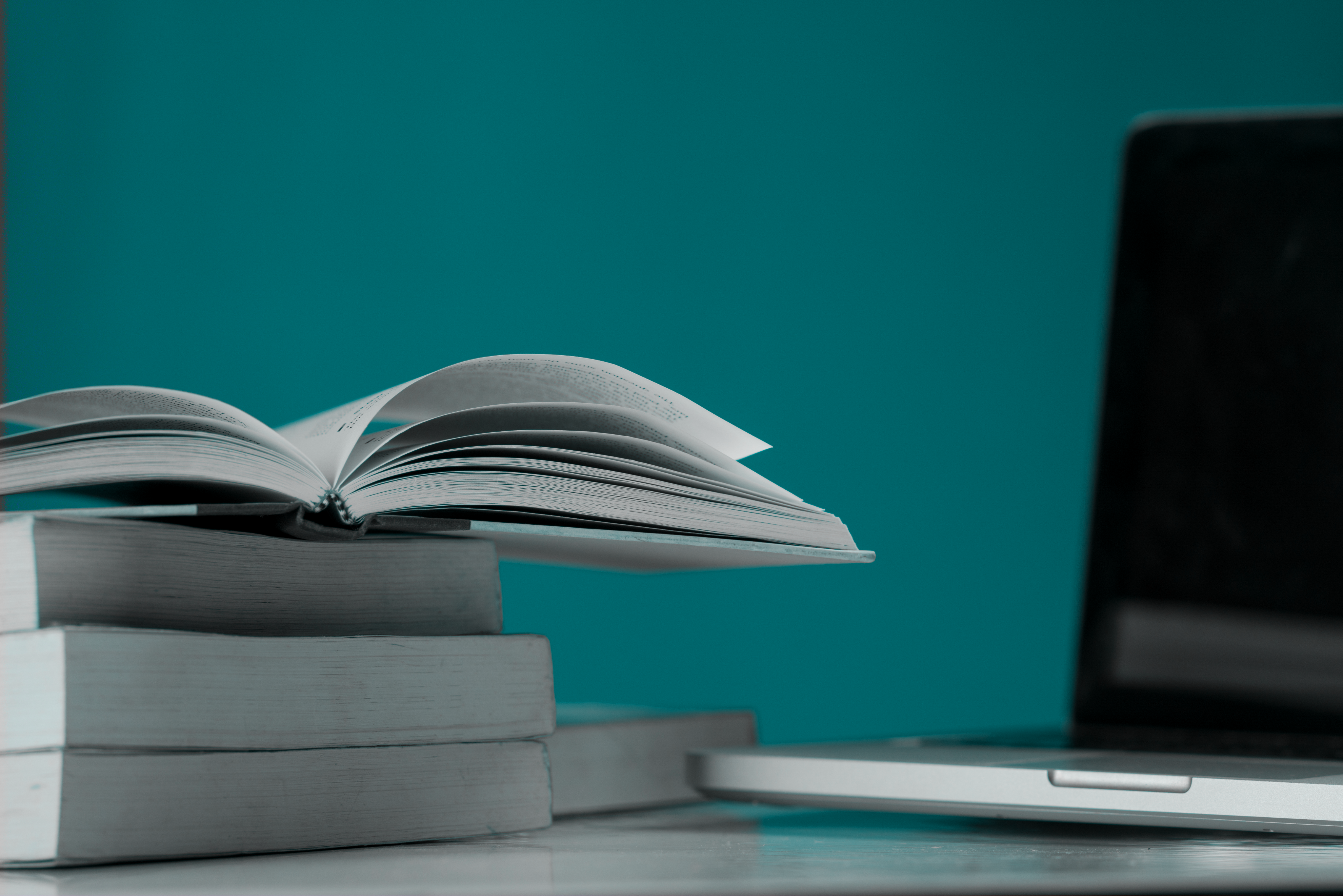 À gauche, un livre ouvert sur une pile de livres, à droite, un ordinateur portable.